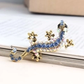 Broche lézard dorée avec cristaux bleu foncé et strass irisés sur un livre - Petit Bleu Clair