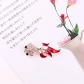 Detailed macro view of goldfish brooch with red enamel tail and sparkling rhinestones - Red