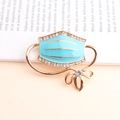 Light blue enamel face mask brooch with white crystals and a gold metal bow pin - Light Blue Mask (5038530716465) / Lake Blue