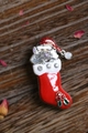 Dettaglio della spilla gatto di Natale in calza rossa su elegante fondo in legno scuro - Rosso