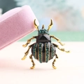 Golden beetle brooch with green rhinestones and black enamel detail on pink velvet box - Green