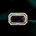 Detail eines luxuriösen Goldrings mit lila Edelstein im Smaragdschliff und grünen Herzen - Lila