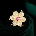 Macro detail of a gold flower brooch featuring white zircon petals and a pink center stone - Pink