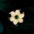 Macro shot of luxury gold flower brooch with pavé petals and large green gemstone - Green