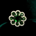 Vista macro de un broche floral dorado de lujo con piedras verde esmeralda y detalles de circón - Tb798