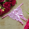 Sexy rosa Tanga aus floraler Spitze mit Satin-Schleifen auf braunem Hintergrund - Rosa