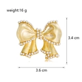 Vista macro della spilla a fiocco con perle bianche e finitura oro opaco, misura 3,6x3,4 cm - C385-a