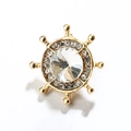 Gros plan de la broche gouvernail dorée ornée d'un cristal central et de petits strass - Or
