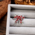 Vue macro d'une broche nœud argentée avec strass rouges et accents de cristaux AB - Argent Rouge