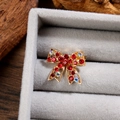 Vue détaillée d'une broche nœud en strass rouges sur base dorée et velours - Or Rouge