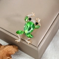 Makroaufnahme einer vergoldeten Froschbrosche mit smaragdgrünen Kristallen - Smaragdgrüner Kristall Frosch Stil