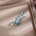 Macro view of silver violin brooch with green crystals on champagne velvet background - Silver Green