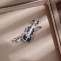 Macro detail of silver violin brooch with deep blue crystals on champagne silk - Silver & Blue