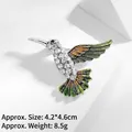 Detail of hummingbird brooch featuring pavé crystals and green enamel wings on white decor - Green Hummingbird (XZ24098)