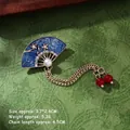 Detail of fan-shaped brooch with blue enamel, white pearl, and golden chain tassels - Blue