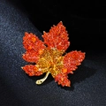 Macro detail of luxury maple leaf brooch with gradient crystals and gold metal finish - Orange