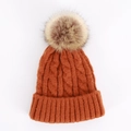 Close-up of thick cable knit texture and faux fur pompom on rust red winter beanie - One Size / Caramel color