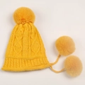 Detail of cable knit pattern and soft poms on a warm ginger yellow chenille winter hat - Yellow