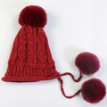 Detailed cable knit texture of a wine red winter hat featuring three soft pom-poms - Red