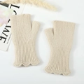 Close-up of cream knit fingerless gloves with ribbed texture and ruffled edge details - Beige