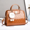 Glossy caramel brown quilted handbag with gold handle and plush charm on white surface - Earthy Yellow