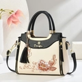 Detail of floral embroidery on cream leather handbag with black tassel and cat charm - Black