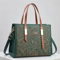 Détail de broderie florale et fermoir doré sur un sac bandoulière vert foncé - Vert