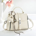 Detailed macro view of cream textured leather handbag with silver rotary lock and mini charm - Off White