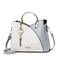 Close-up of color-block leather handbag with gold metal handle and heart tassel charm - Sky Blue & White