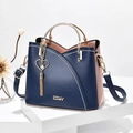 Detailansicht der Handtasche mit Kontrastfarben, Herzanhänger und goldenen Metallteilen - Blau