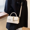 Detail of a creamy white rectangular handbag with glossy finish and gold metal buckle - White
