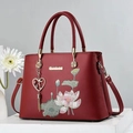 Elegant wine red handbag with lotus embroidery and metallic tassel on display - Burgundy
