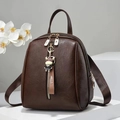 Detalle de mochila de cuero marrón oscuro con cremalleras doradas y colgante decorativo - Café
