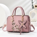 Detail of dusty rose handbag with floral embroidery and floral charm on white stand - Pink