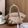 Detalle del bolso de ala en cuero granulado con un colgante de cachorro sobre fondo madera - 28*7*14 / Caqui