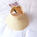Detail of yellow and white striped woven straw sun hat with decorative bow on white fabric - Yellow