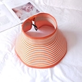 Detail of orange and white striped straw sun hat with adjustable strap on white fabric - Orange