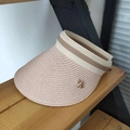 Detailed close-up of straw sun visor with gold bee pin on wooden display stand - Pink