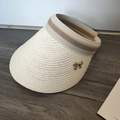 Detail van witte strooien zonneklep met gouden strikgesp en gestreepte geweven band - Crèmewit