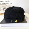 Detail of black corduroy docker hat featuring side woven label and metal buckle hardware - Black