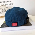 Close-up of blue corduroy docker hat with red tag and adjustable metal strap - Blue