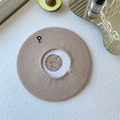 Close-up of knit beret in khaki with a decorative letter P patch on textured surface - One Size / Beige Khaki