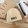 Detailed view of cream knit beanie with black 1011 numeric embroidery on soft wool texture - 55-58cm / Beige