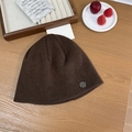 Dark brown knitted beanie with silver metal logo tag on a warm wood background - 56-58cm / Brown