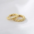 Detail von goldenen gedrehten Creolen mit Zirkonia-Mikroinlay auf weißem Textilhintergrund - 925er Silber / Gold