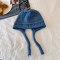 Blue knitted aviator beanie with long earflap ties on white textured fabric background - Blue