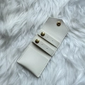 Detail view of portable cream PU leather jewelry pouch with gold snap buttons and earring slots - White