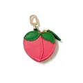 Detailed view of peach-shaped pink leather coin purse with green leaves and gold hook - Peach