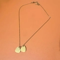 Détail d'un collier pendentif cœur en or sur un fond texturé de couleur orange - Double Cœur / Doré