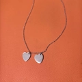Gros plan du collier à double pendentif en forme de cœur sur fond en cuir orange - Double Cœur / Argenté
